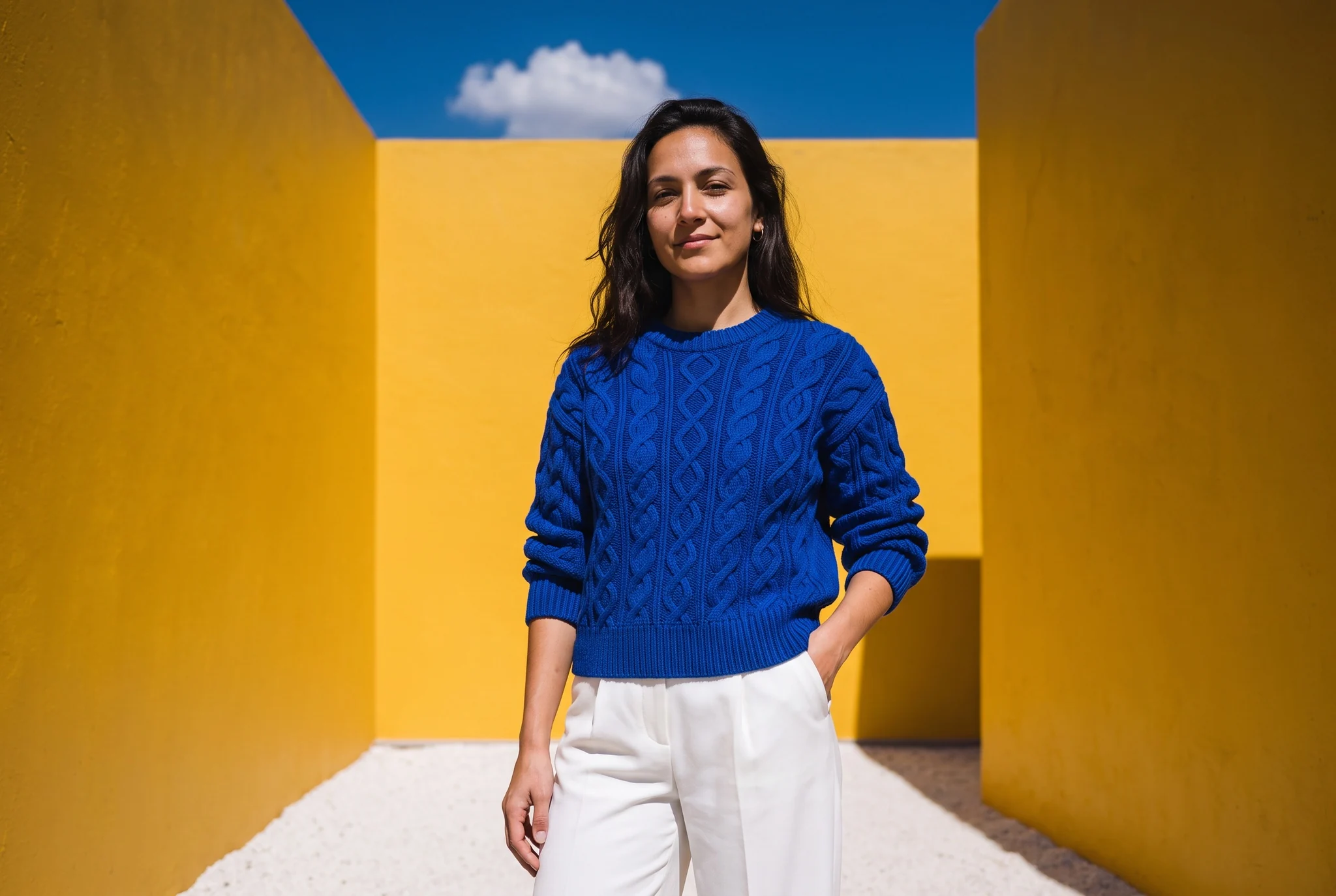 Cobalt cable-knit jumper worn in a sunlit yellow courtyard
