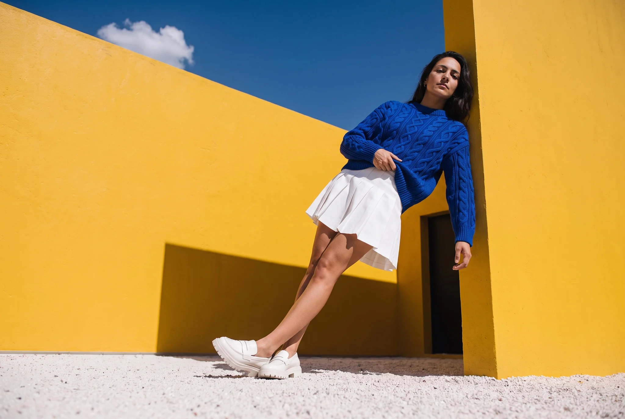 Cobalt cable-knit jumper, portrait against yellow walls