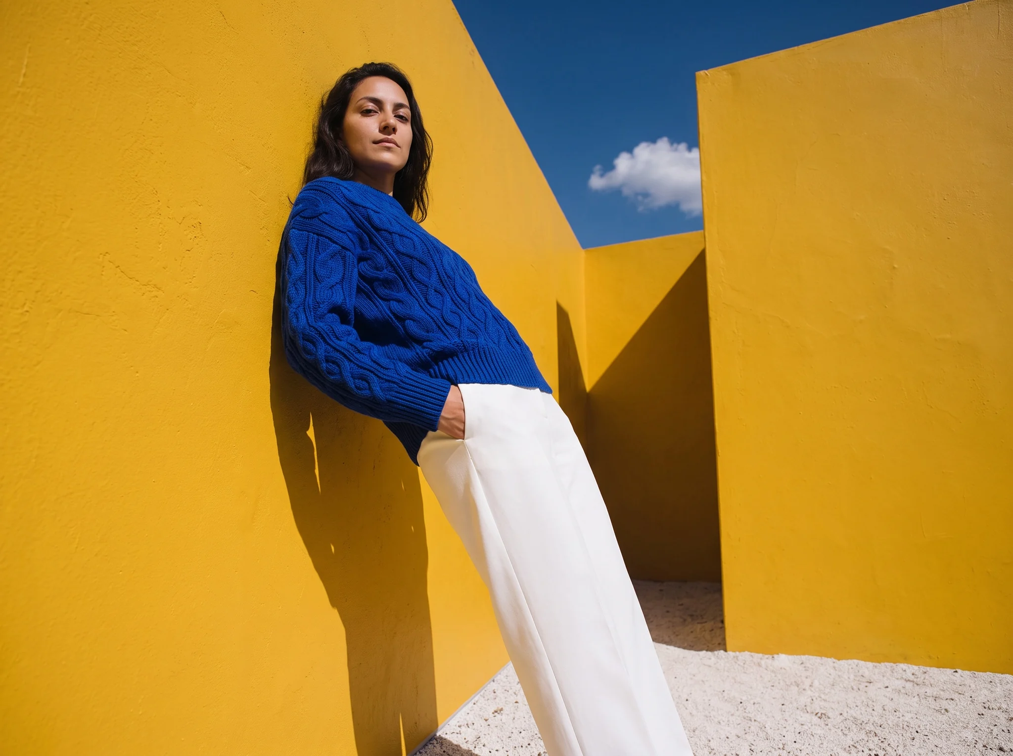 Portrait of the cobalt cable-knit jumper in a yellow courtyard